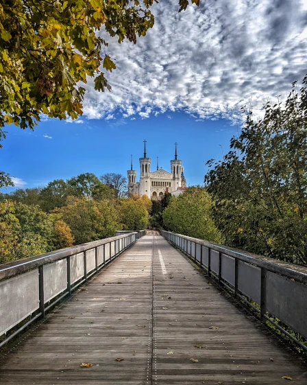 A long perspective shot of a bridge high amongst the trees leading to The Basilica of Notre-Dame de Fourvière in Lyon, France