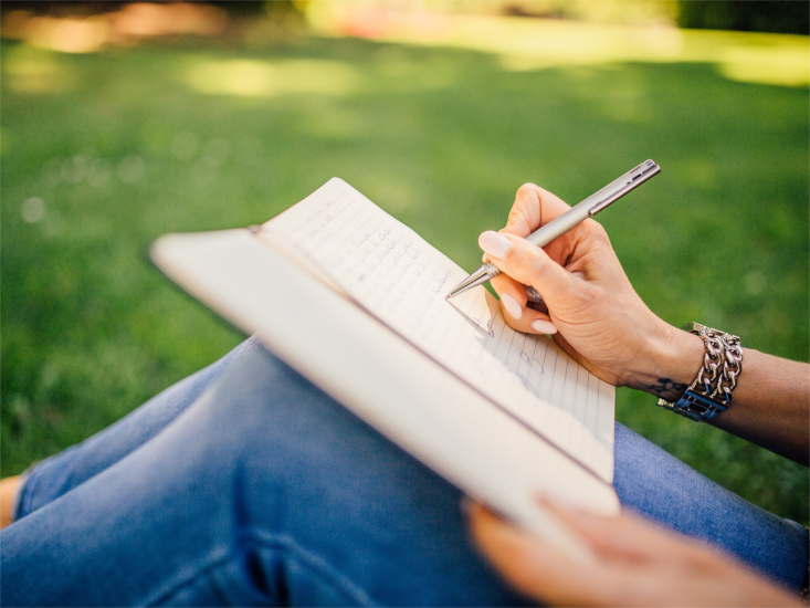 Image of a woman writing in a notebook in the park.