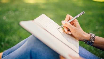 Image of a woman writing in a notebook in the park.
